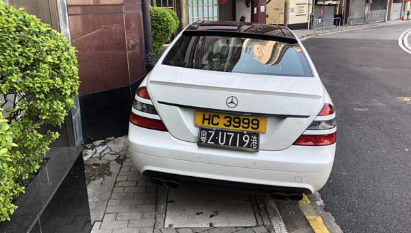 A white Mercedes with Hong Kong and mainland China plates completely blocks a Hong Kong sidewalk